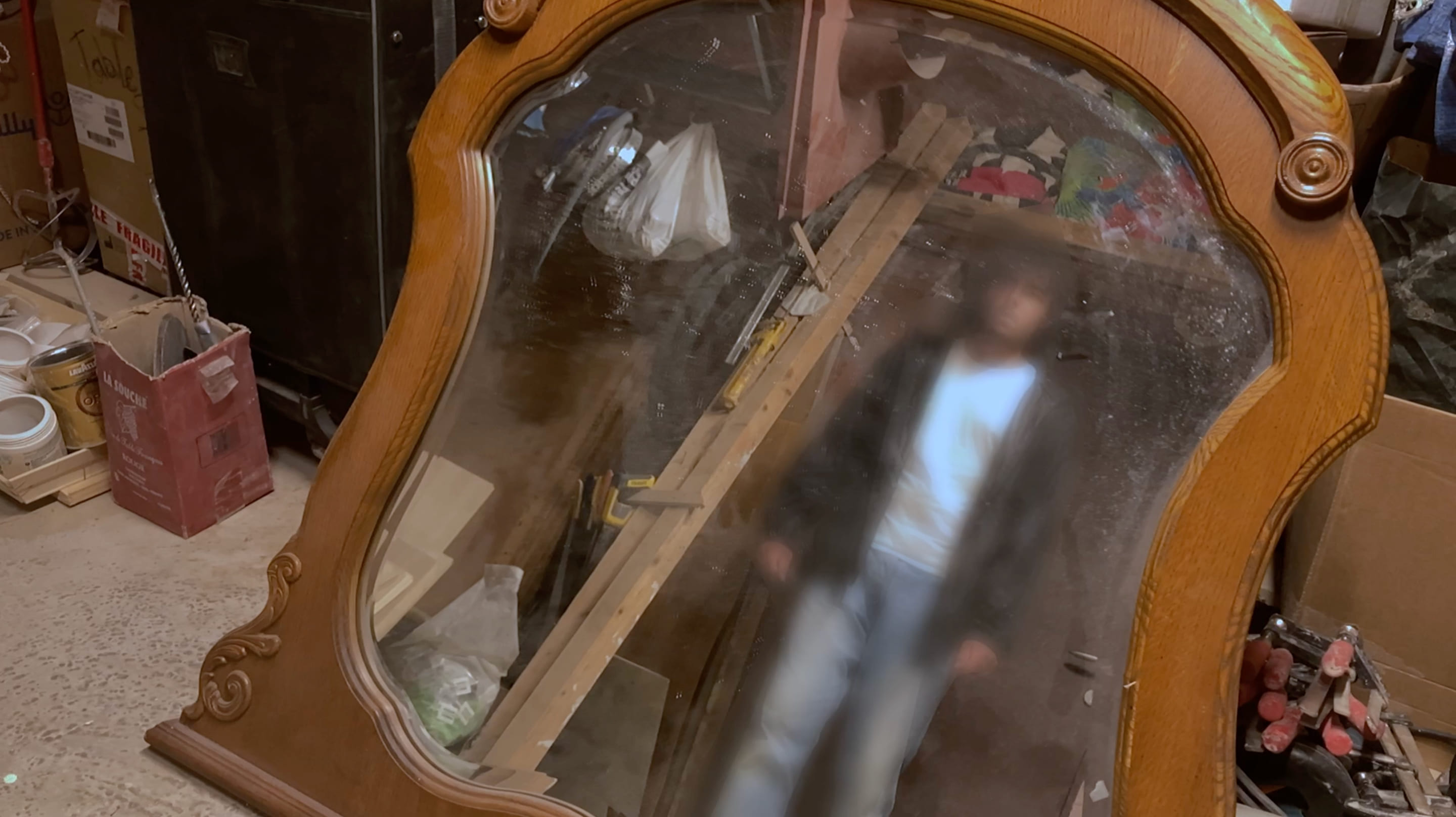 4e photographie de Shattered Reality où un homme regarde son reflet dans un grand miroir posé sur le sol. Autour du miroir se trouvent différents cartons et outil de constructions. L'homme en question est flou.